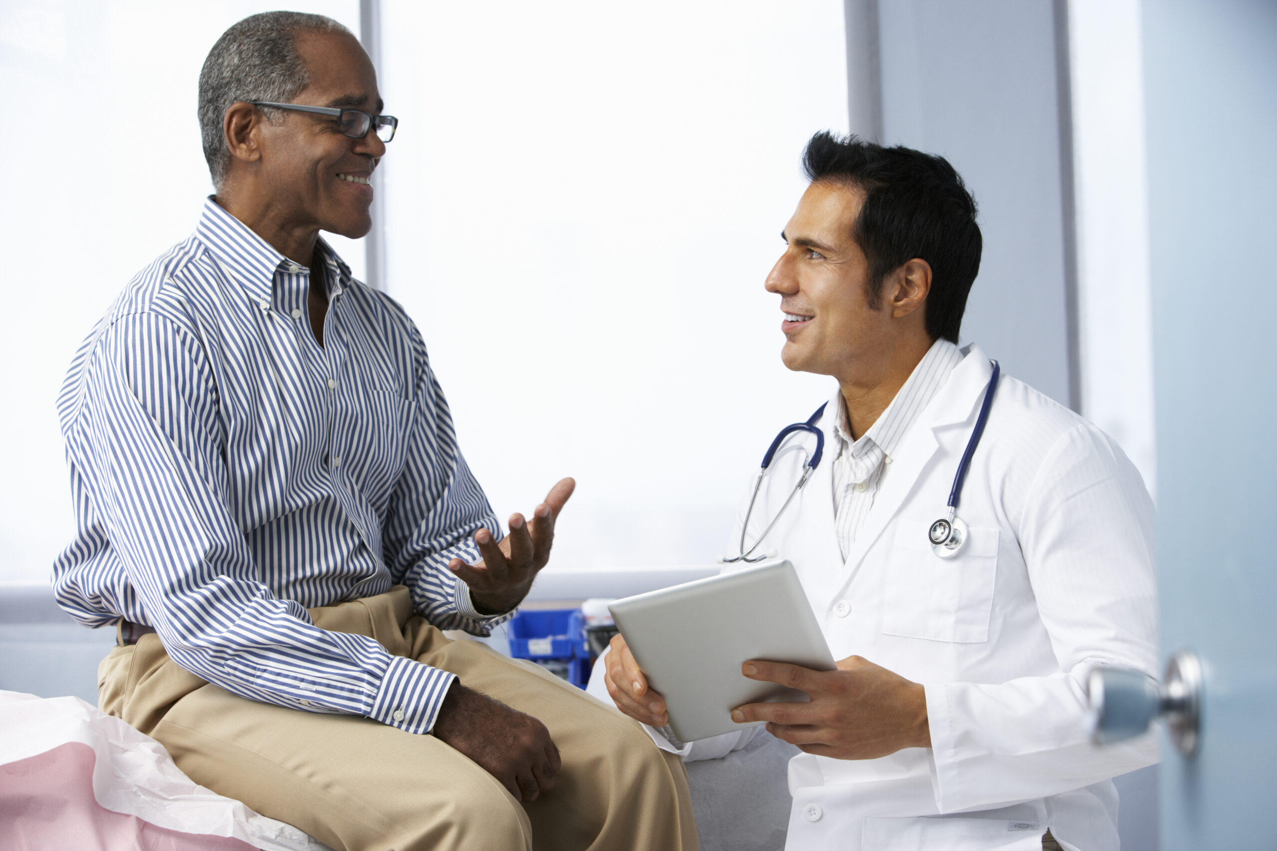 Doctor In Surgery With Male Patient Using Digital Tablet